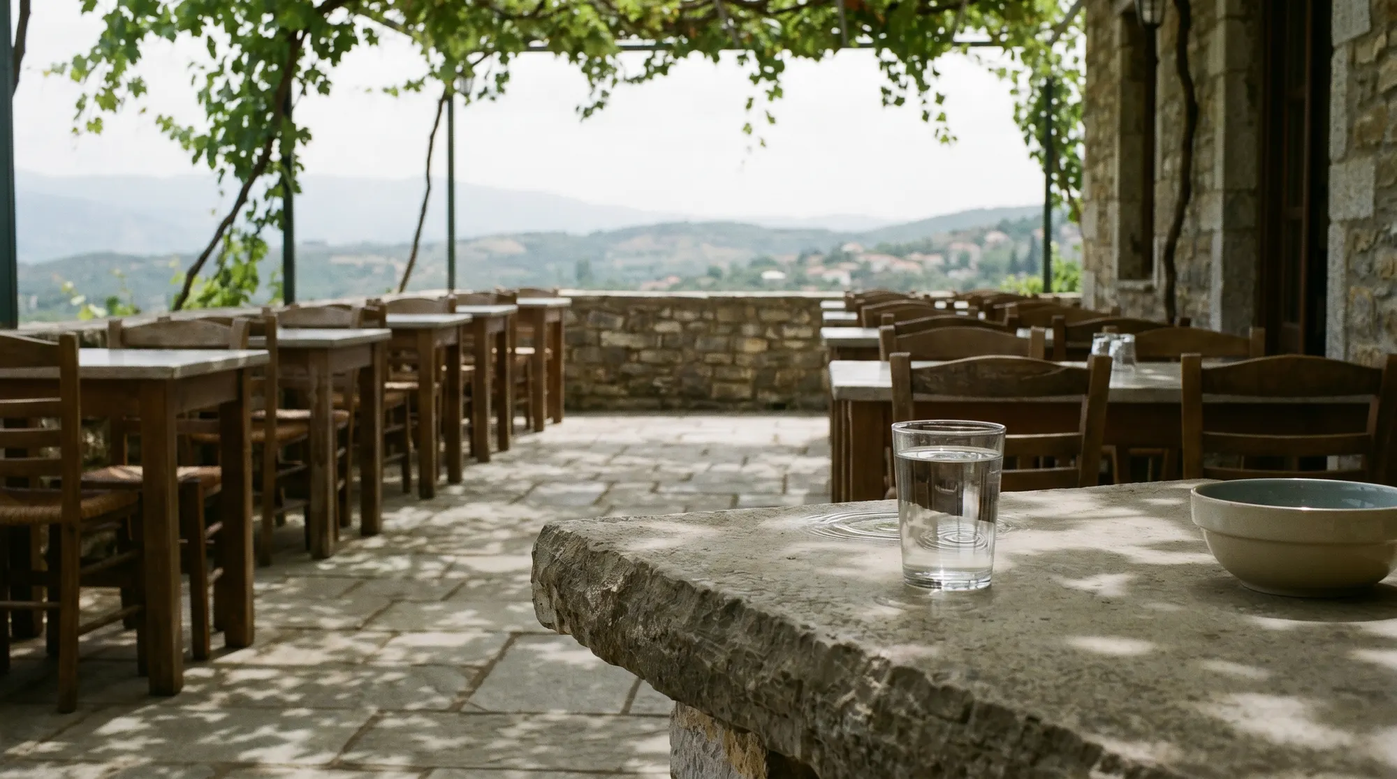 The vine-shaded stone terrace of Beit Ward at golden hour, tables set, olive groves and mountains beyond
